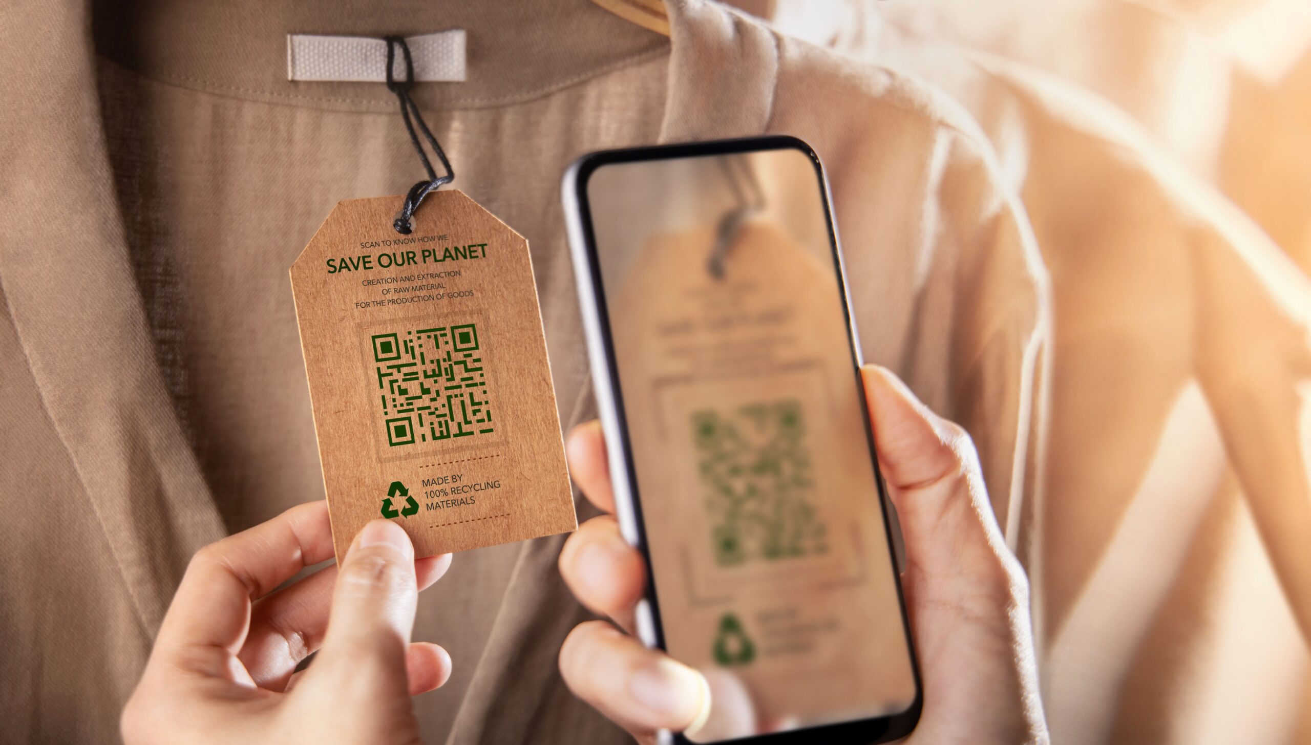 Person scannt QR-Code an Kleidungsetikett mit Hinweis auf Recycling bei nachhaltiger Mode
